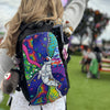 Close-up of a festival-goer wearing a black Lunchbox hydration pack with the "Funkonaut" skin, featuring a psychedelic astronaut floating through colorful swirling dimensions, decorated with a plush donkey charm and a sprout clip.