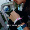 Close-up of a person refilling the hydration pack bladder of the black Lunchbox Hydration Sling at a festival water refill station with the text EASY WATER REFILL