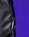 Extreme close-up of the black Lunchbox Phone Satchel focusing on the heavy-duty metal anti-theft zipper clip secured to a reinforced fabric loop against a purple background.