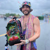 Festival attendee wearing a patterned bucket hat and scarf holding up a Lunchbox hydration backpack featuring the EDC Orlando 2026 skin