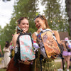 Two friends showing off their custom Lunchbox hydration packs with colorful designs at a music festival