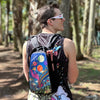 A festival attendee wearing a Lunchbox Packs hydration backpack with the colorful "Which Way To Roo" skin at Bonnaroo 2026, featuring vibrant space-themed art and planet illustrations.