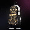 A white Lunchbox hydration pack with a black and gold EDC Las Vegas 2025 skin attached to the front. The skin features a gold Art Deco "EDC" logo, "All Are Welcome Here" text, and floral smiley face patterns. The pack is set against a dark background with a pink glowing wave and the Insomniac and Lunchbox logos at the bottom.