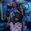 A smiling person at a festival holding up a peace sign while wearing a black Lunchbox Hydration Sling with the hydration hose attached.