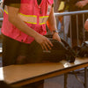 Close-up of a person in a pink safety vest inspecting the black Lunchbox Hydration Sling on a table at an event security checkpoint.