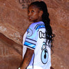 Side profile view of woman wearing limited edition white and purple Lunchbox festival baseball jersey outdoors at Red Rocks.