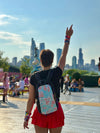 Rear view of a person wearing a Lunchbox Lollapalooza hydration pack with colorful skin pointing at the Chicago skyline